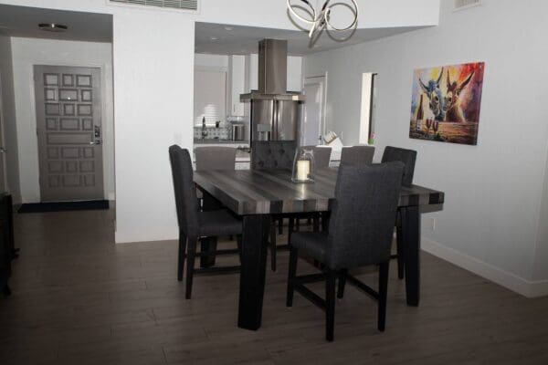 A dining room table with black chairs and a painting on the wall.